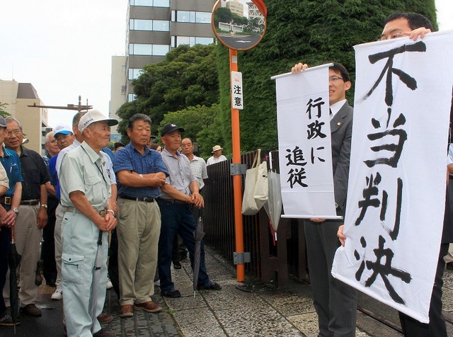 「不当判決」「行政に追従」と書いた紙を掲げる弁護士（右）と原告漁協の人たち=7月17日、水戸地裁前