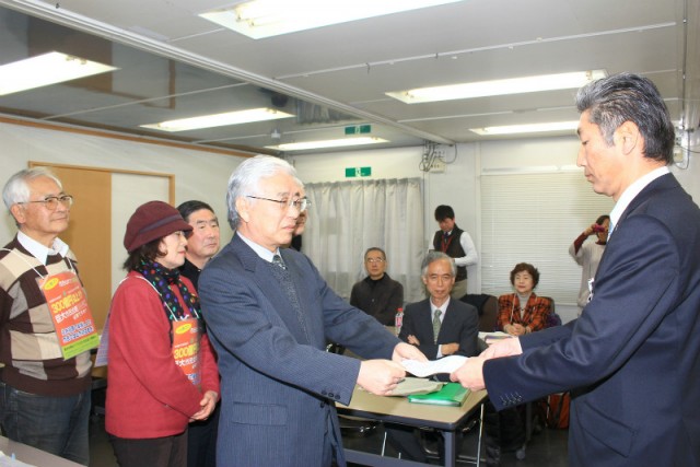 市長あての交付申請書を市担当部長（右）に手渡す「市民の会」の田中代表=2月3日、水戸市役所